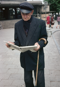 849504 Afbeelding van een man die de krant leest op het Stationsplein te Utrecht.